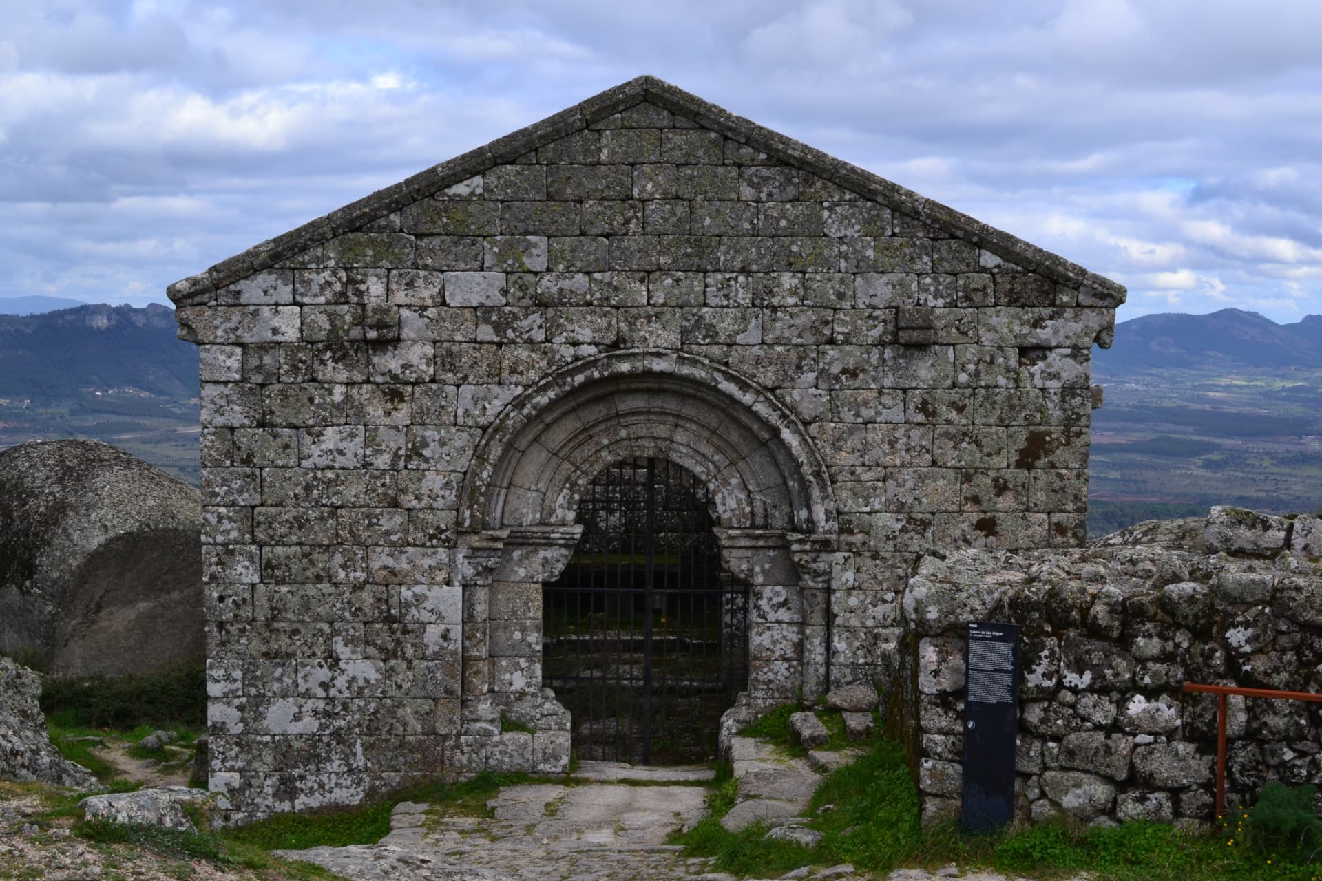 Fachada da capela românica de São Miguel em pedra, com montanhas ao fundo