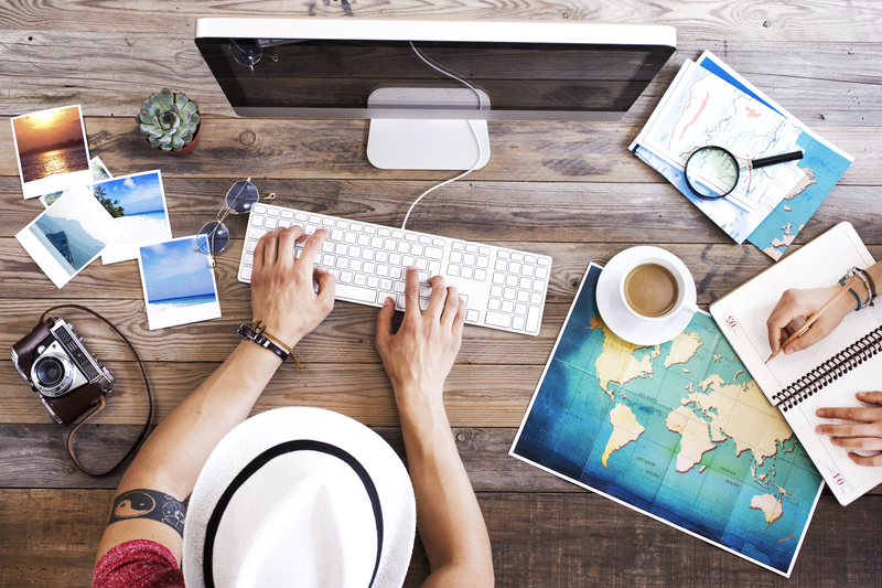 Mesa de planeamento de viagem vista de cima, com computador, mapa do mundo, câmara fotográfica, fotos de destinos, café e caderno de notas