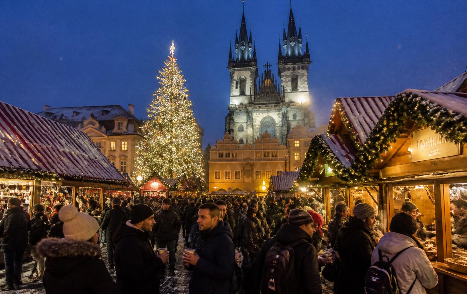 Praça histórica europeia com barracas de madeira, árvore iluminada e neve durante um mercado de Natal