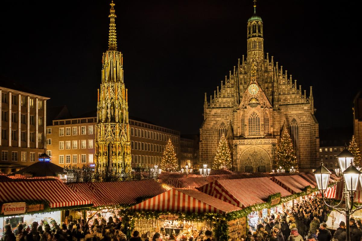 Christkindlesmarkt de Nuremberg na Hauptmarkt, com barracas de toldo vermelho e branco, a Frauenkirche e a fonte Schöner Brunnen iluminadas